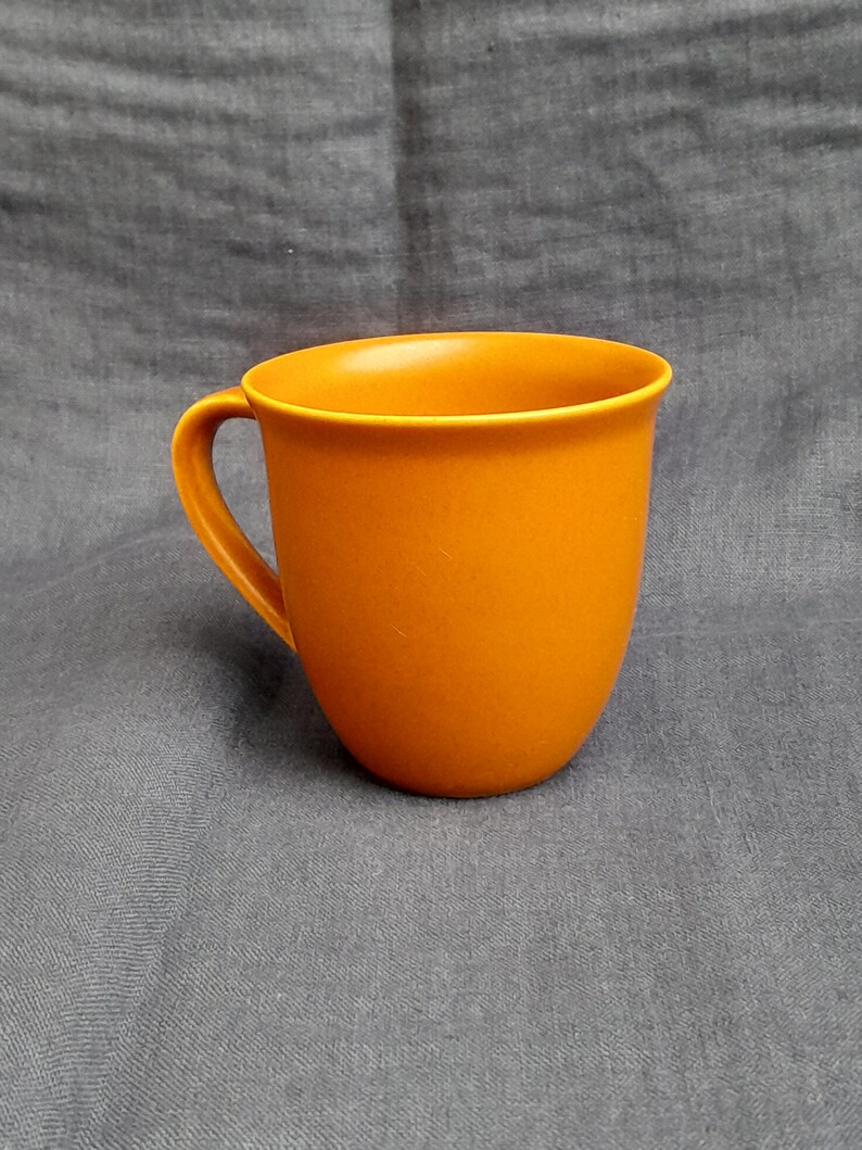 May include: A solid orange ceramic mug with a rounded handle.
