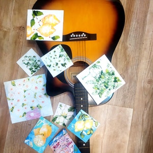May include: A brown acoustic guitar with a black neck and strings. The guitar is surrounded by small paintings with floral and citrus fruit designs.