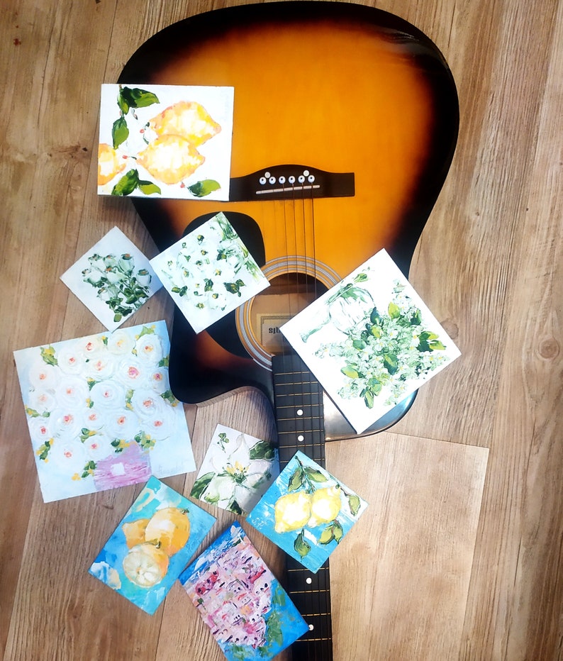 May include: A brown acoustic guitar with a black neck and strings. The guitar is surrounded by small paintings with floral and citrus fruit designs.