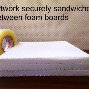 May include: Two white foam boards stacked on top of each other. The boards have a textured surface and are secured with tape. The text "Artwork securely sandwiched between foam boards" is visible at the top of the image.