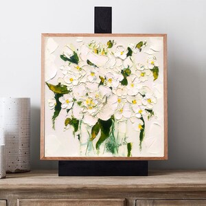 May include: A framed painting of a bouquet of white flowers with yellow centers in a green vase. The flowers are painted in a loose, impressionistic style.