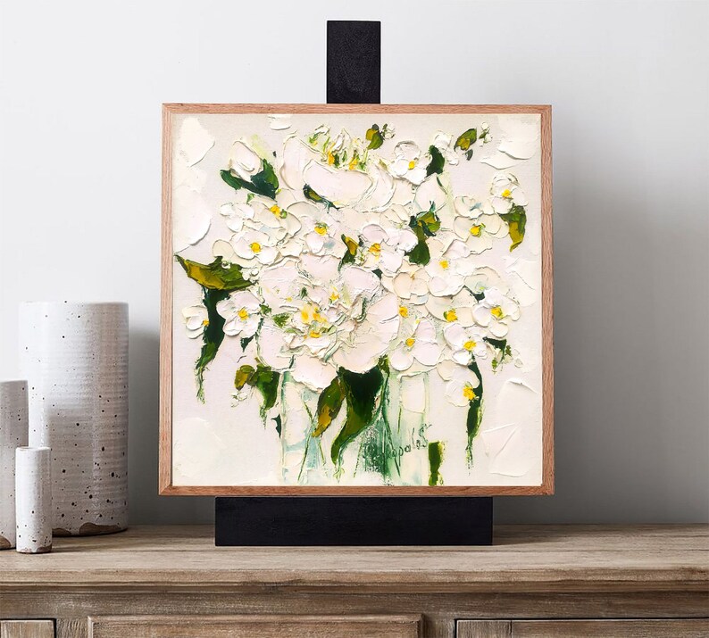 May include: A framed painting of a bouquet of white flowers with yellow centers in a green vase. The flowers are painted in a loose, impressionistic style.