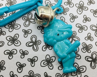 May include: A blue plastic keyring with a silver bell and a blue plastic figurine of a person holding a bat.