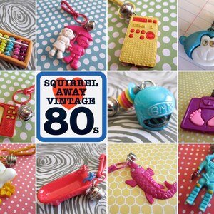 May include: A collection of vintage 1980s plastic charm keychains. The charms include a television, a bathtub, a fish, a robot, a helmet, a scale, a dog and cat, a girl with an umbrella, an abacus, and a radio. The charms are all brightly coloured and have a retro feel.