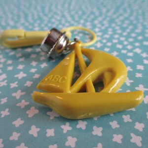 May include: Yellow plastic sailboat charm with a metal clasp and the letters "ABC" on the sail.