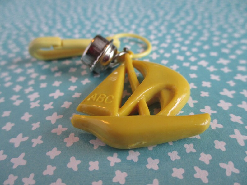 May include: Yellow plastic sailboat charm with a metal clasp and the letters "ABC" on the sail.