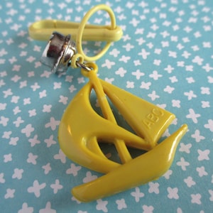 May include: A yellow plastic sailboat keyring with a metal ring and a silver clip. The sailboat has the letters "ABC" printed on the side.