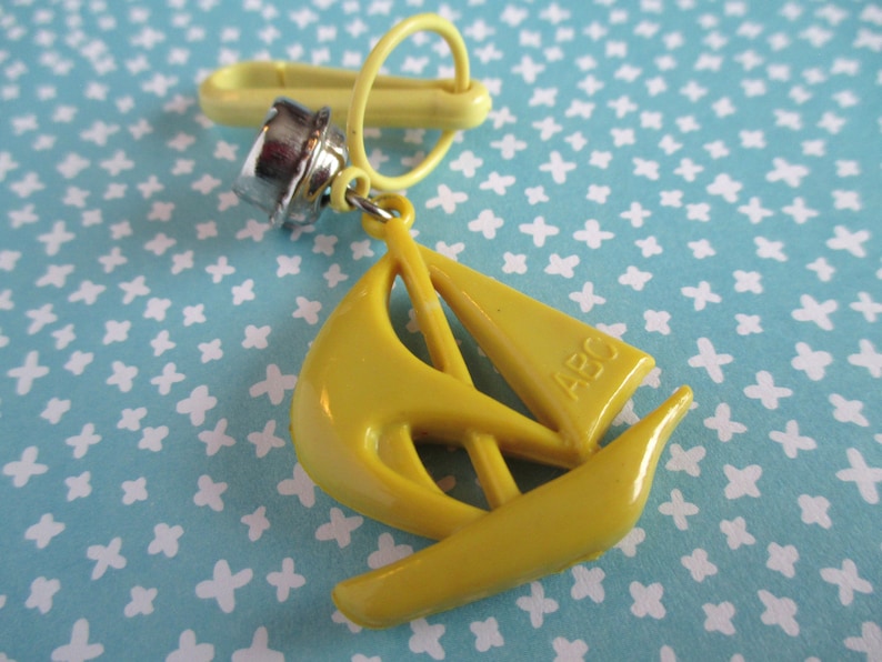 May include: A yellow plastic sailboat keyring with a metal ring and a silver clip. The sailboat has the letters "ABC" printed on the side.