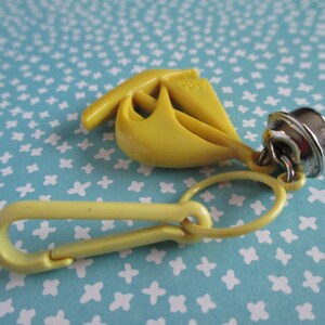 May include: Yellow plastic sailboat keyring with a silver bell charm and a yellow plastic clip.