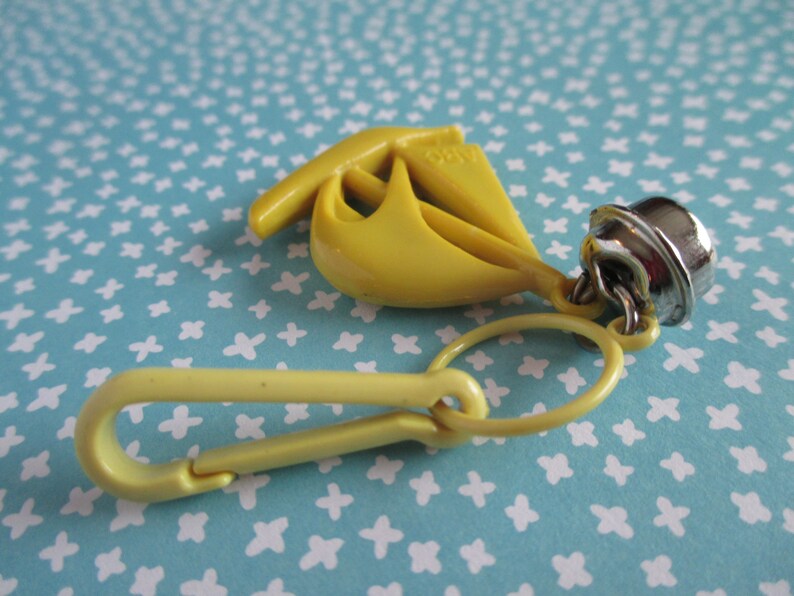 May include: Yellow plastic sailboat keyring with a silver bell charm and a yellow plastic clip.