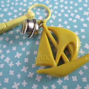 May include: A yellow plastic sailboat charm with the letters "ABC" on the sail. The charm is attached to a yellow plastic clip.