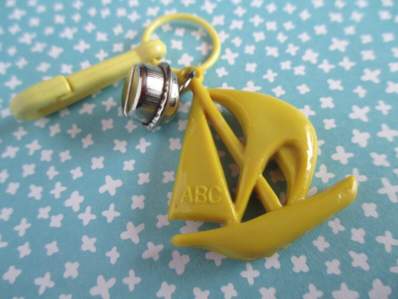 May include: A yellow plastic sailboat charm with the letters "ABC" on the sail. The charm is attached to a yellow plastic clip.