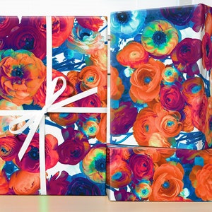 May include: Three gift boxes wrapped in colorful floral patterned paper. The paper features a vibrant mix of orange, red, blue, and purple flowers. The boxes are tied with white ribbon.