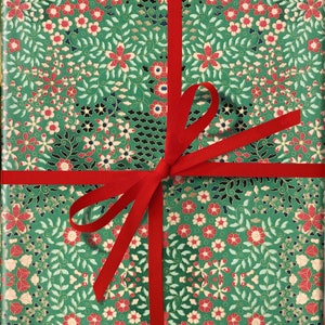 May include: A green gift box with a red ribbon and bow. The box is wrapped in paper with a floral pattern.