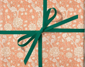 May include: A peach-colored gift box with a floral pattern is tied with a green ribbon. The ribbon is tied in a bow on top of the box.
