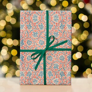 May include: A gift wrapped in white paper with a blue and red floral pattern. The paper is tied with a green ribbon and bow.