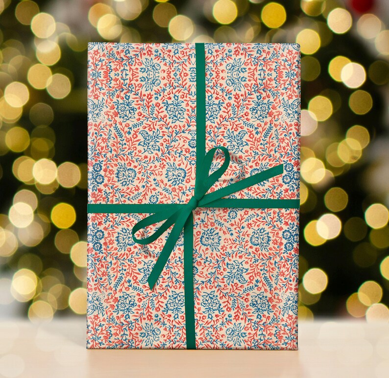 May include: A gift wrapped in white paper with a blue and red floral pattern. The paper is tied with a green ribbon and bow.