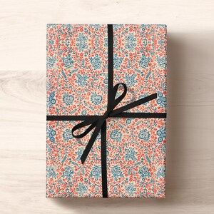 May include: A gift wrapped in white paper with a red and blue floral pattern. The paper is tied with a black ribbon and bow.