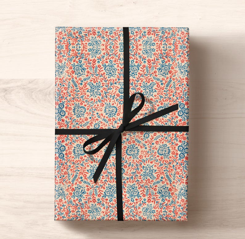 May include: A gift wrapped in white paper with a red and blue floral pattern. The paper is tied with a black ribbon and bow.
