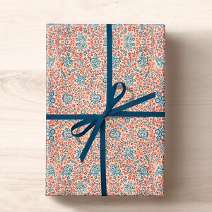 May include: A gift wrapped in white paper with a blue and red floral pattern. The paper is tied with a blue ribbon and bow.