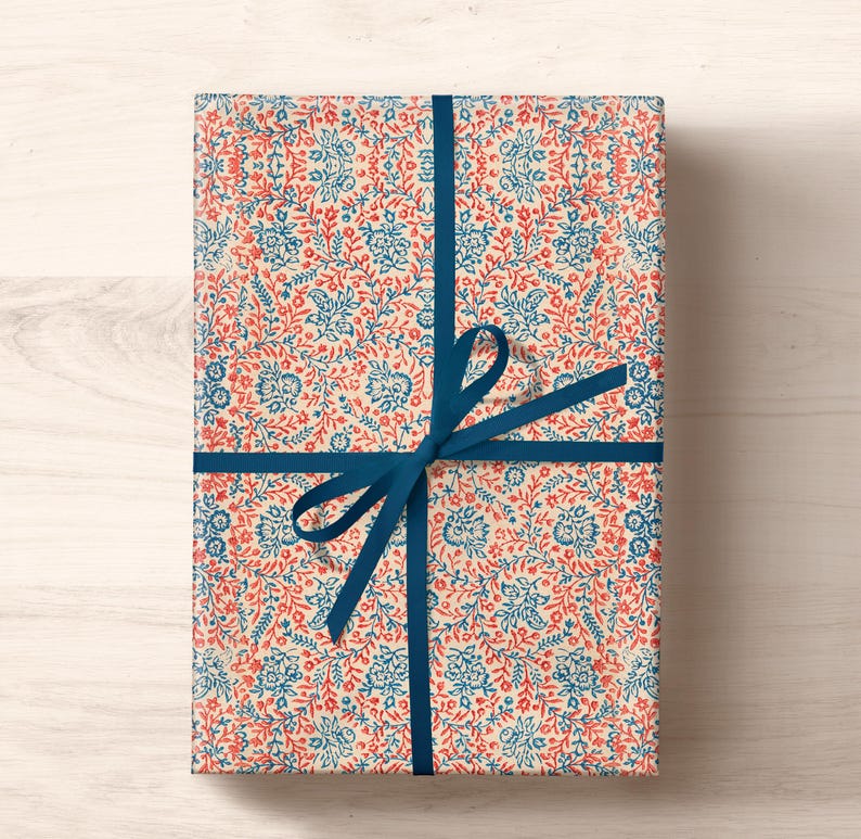 May include: A gift wrapped in white paper with a blue and red floral pattern. The paper is tied with a blue ribbon and bow.
