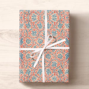 May include: A gift wrapped in cream-colored wrapping paper with a blue and red floral pattern. The gift is tied with a white ribbon.
