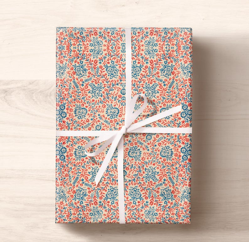 May include: A gift wrapped in cream-colored wrapping paper with a blue and red floral pattern. The gift is tied with a white ribbon.