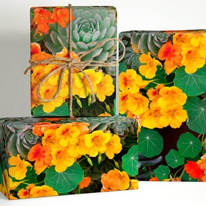 May include: Three gift boxes wrapped in floral patterned paper. The paper features yellow and orange flowers, green leaves, and succulents. The boxes are tied with twine.