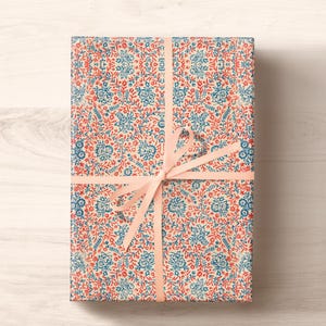 May include: A gift wrapped in white paper with a blue and red floral pattern. The gift is tied with a pink ribbon.