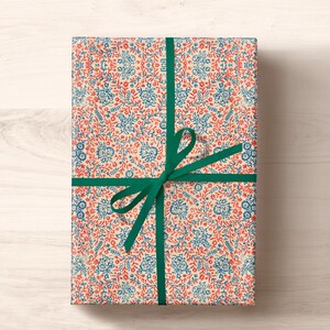 May include: A gift wrapped in white paper with a blue and red floral pattern. The gift is tied with a green ribbon.