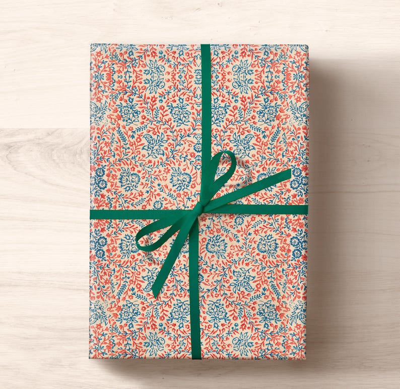 May include: A gift wrapped in white paper with a blue and red floral pattern. The gift is tied with a green ribbon.