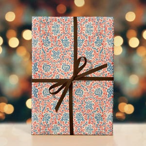 May include: A gift wrapped in white paper with a red and blue floral pattern. The paper is tied with a brown ribbon and bow.