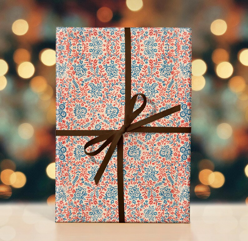 May include: A gift wrapped in white paper with a red and blue floral pattern. The paper is tied with a brown ribbon and bow.