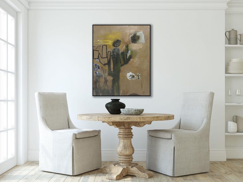 Puede incluir: Pintura abstracta en tonos de marr&oacute;n, verde y blanco con l&iacute;neas negras. La pintura est&aacute; enmarcada en negro y colgada en una pared blanca sobre una mesa de madera con dos sillas.