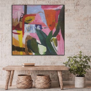 May include: Abstract painting with bold strokes of pink, orange, yellow, green, and blue. The painting is framed in black and hangs on a white brick wall.