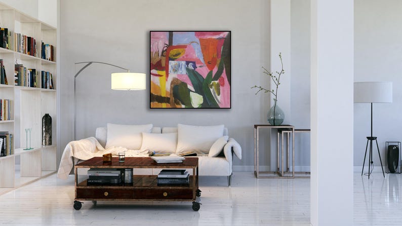 May include: Abstract painting with pink, green, yellow, and blue colors. The painting is framed and hanging on a white wall in a living room setting.