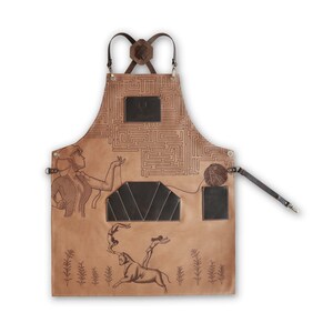 May include: A brown leather apron with a maze pattern, a woman figure, and a bull with two figures on its back. The apron has two pockets and adjustable straps. The text "The Maker" is printed on the apron.