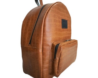 Pode incluir: Uma mochila marrom de couro sintético com padrão de crocodilo. A mochila tem um bolso frontal com zíper e uma etiqueta preta com a palavra "MODERN" nela.