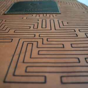 May include: A brown leather apron with a black maze pattern and a small brown leather patch with the word "Nesso" embossed on it.