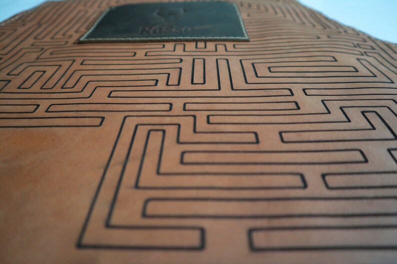 May include: A brown leather apron with a black maze pattern and a small brown leather patch with the word "Nesso" embossed on it.