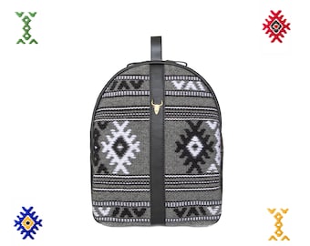 Pode incluir: Uma mochila cinza e preta com padrão geométrico, alça de couro preta e um detalhe de cabeça de touro dourada.