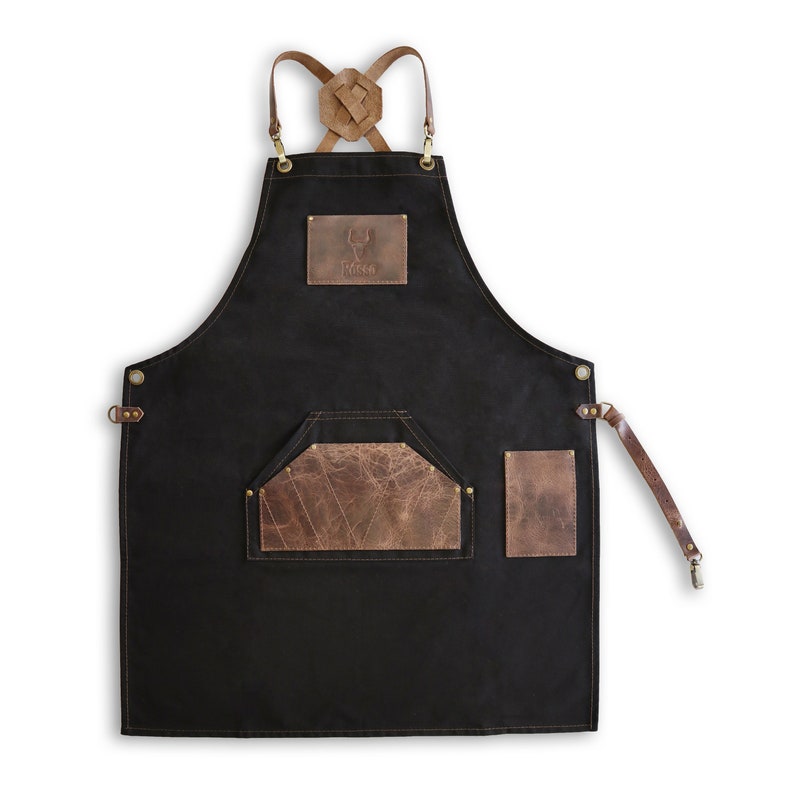 May include: Black canvas apron with brown leather straps, a large brown leather pocket, and a smaller brown leather pocket on the right side. The apron has a brown leather patch with a stag logo and the word "RIDGE" embossed on it.