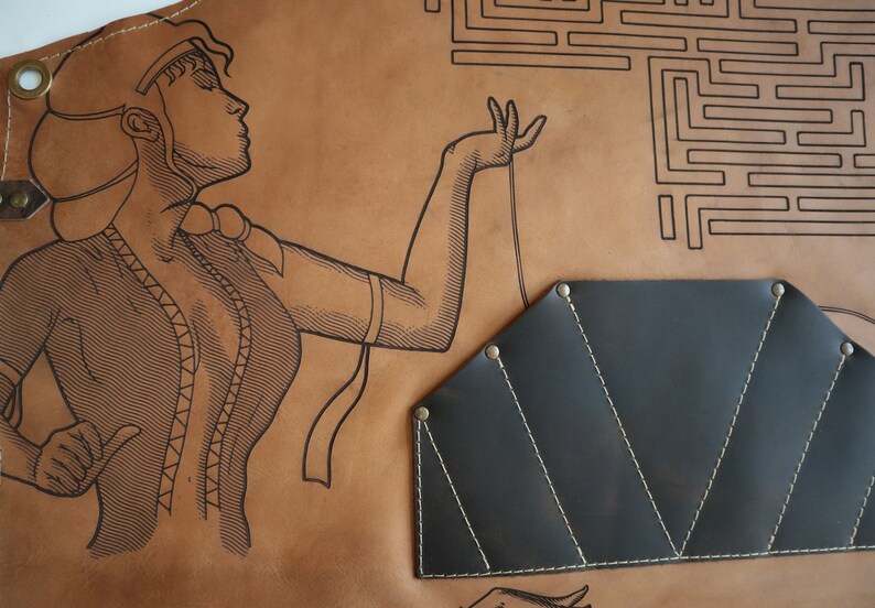 May include: A brown leather apron with a black leather tool pouch. The apron features a line drawing of a woman with a maze in the background.