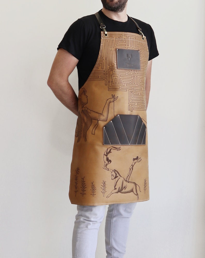 May include: A brown leather apron with a maze pattern and a pocket. The apron has a design of a woman holding a bull's horn and a man jumping over the bull. The apron has a leather patch with the word "Tasco" on it.