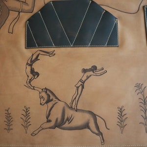 May include: A brown leather apron with a black leather patch and two smaller black leather pockets. The apron has a design of a bull, a woman jumping over the bull, and another woman doing a backflip.