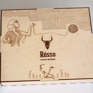 May include: A wooden box with a laser-engraved design. The design features a woman holding a ball of yarn, a bull, and the text "R&aacute;sso exclusive workwear".