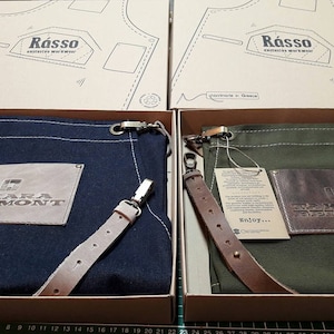 May include: Two canvas aprons with leather straps and a brown leather patch with the text "Takara Belmont" on each. The aprons are in a navy blue and a dark green color. The aprons are in boxes with the text "R&aacute;sso" on the top.