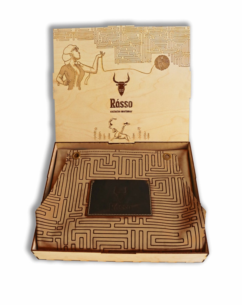 May include: A wooden box with a leather apron inside. The apron has a maze pattern and a leather patch with the word "Rasso" on it. The box lid has a maze pattern and a drawing of a woman holding a ball of yarn.