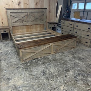 Puede incluir: Una estructura de cama de madera rústica con cabecero, piecero y mesitas de noche. El cabecero presenta un diseño en forma de X. La estructura de la cama y las mesitas de noche son de madera clara con detalles en marrón oscuro. También se ve una cómoda a juego con seis cajones.