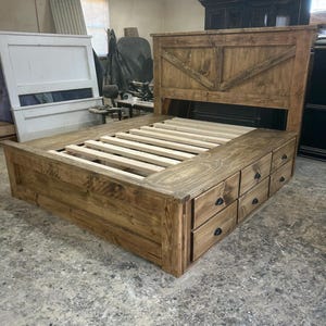 Può includere: Un letto in legno rustico con testiera con design diagonale. Il letto ha una base a piattaforma con più cassetti e un telaio a doghe. Il legno ha una finitura naturale.
